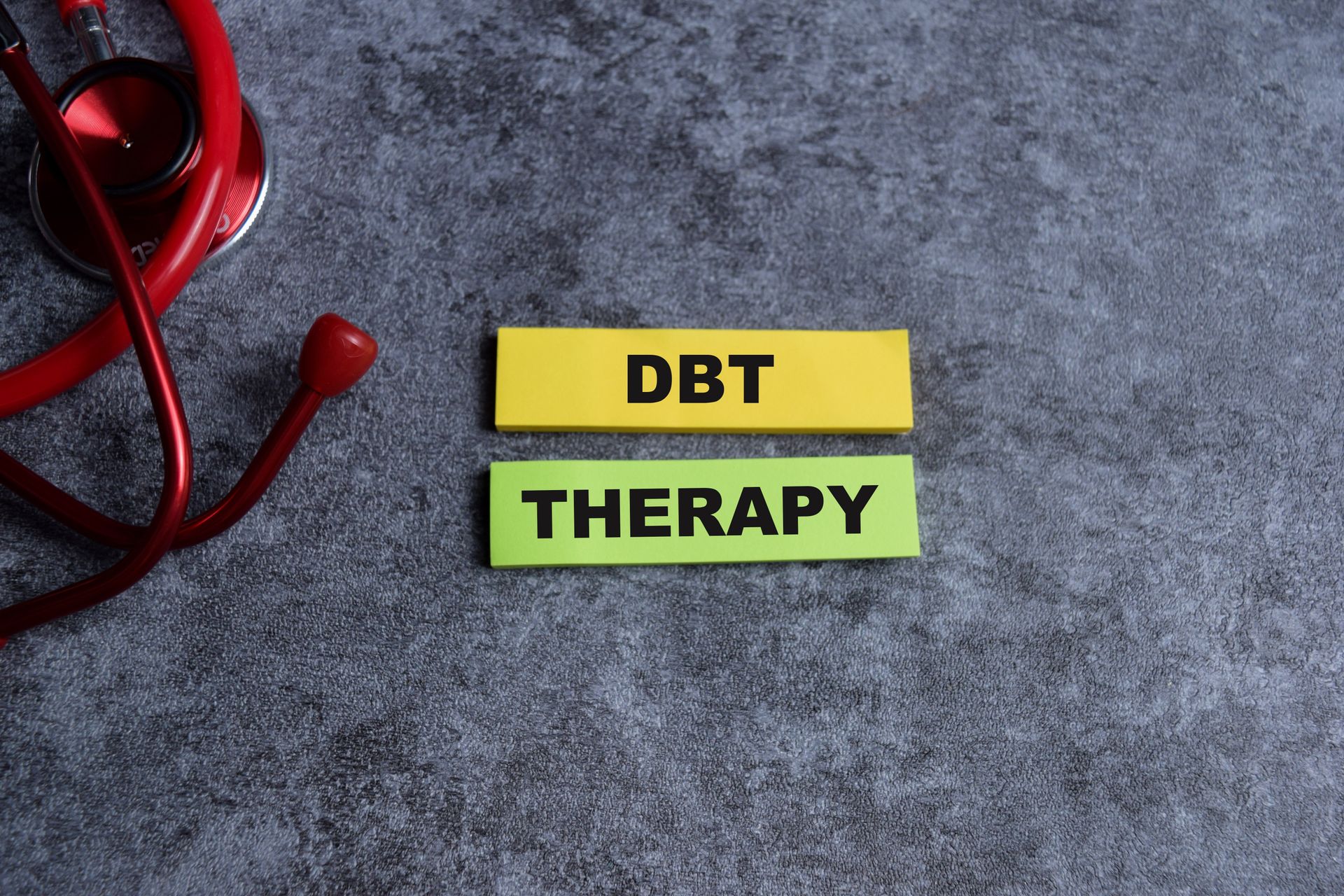 Yellow tiles reading “DBT THERAPY” on a gray background with a red stethoscope