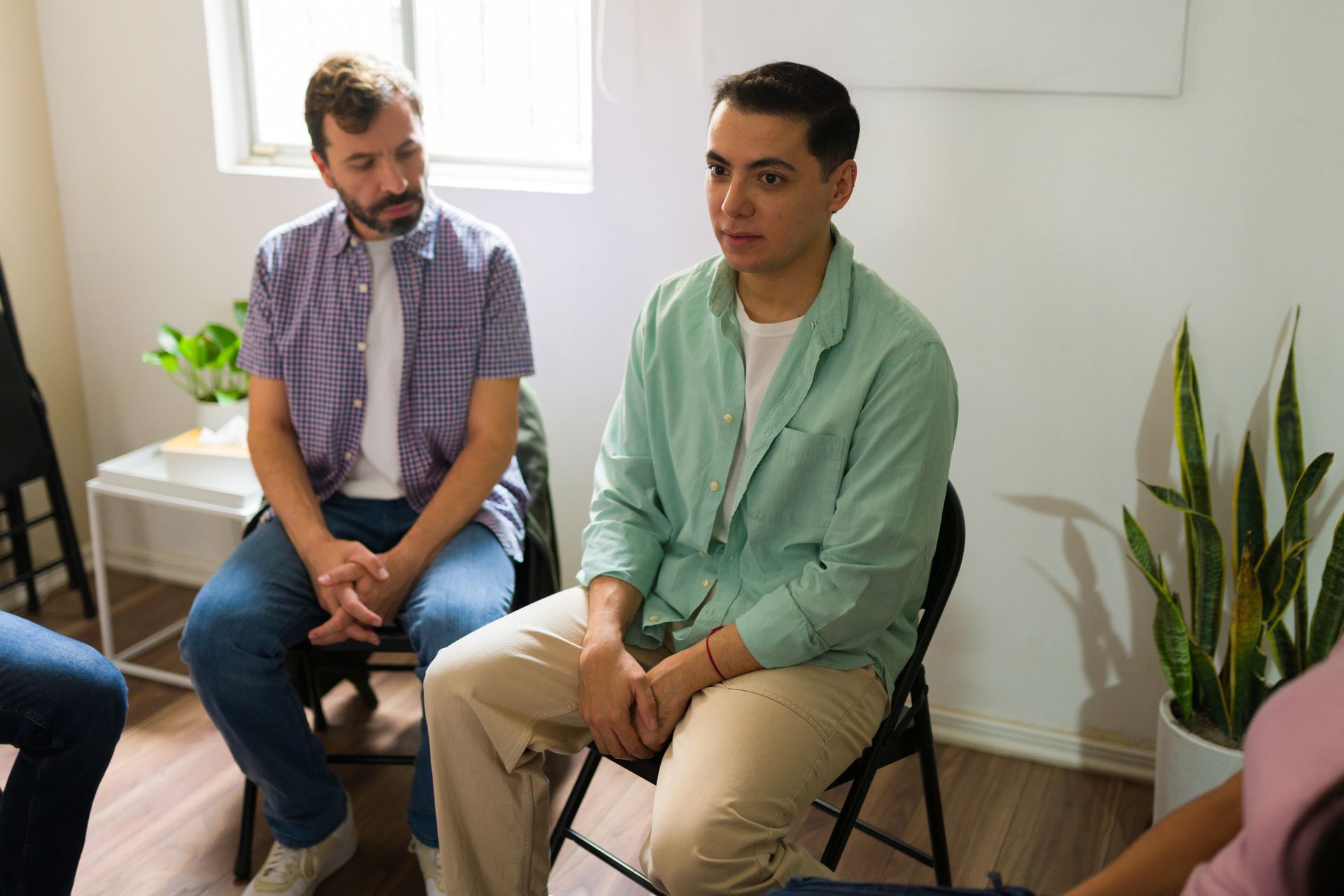 Two people seated in a bright room, talking in a small group setting.