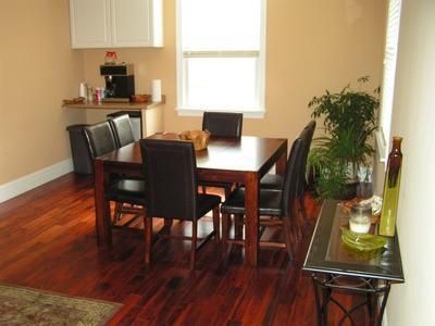A dining room with dark wooden floors, a square table with four black chairs, and a small coffee station against the wall.
