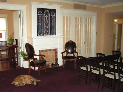 A living room with a fireplace, a dog resting on a carpet, two leather chairs, and a dining table with chairs.