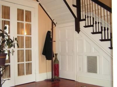 A foyer with white paneled walls and doors, a wooden staircase with dark railings, a coat rack, and a tall decorative vase.