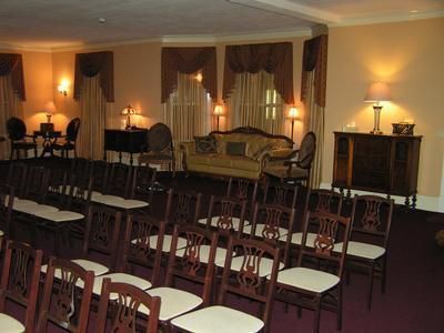 An indoor space arranged with rows of chairs facing a small lounge area with a sofa, lamps, and windows with drapes.