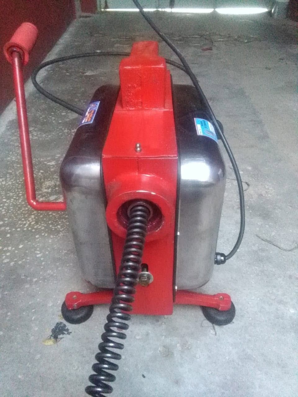 Máquina roja para desatascar desagües con un cable enrollado en el suelo de un taller