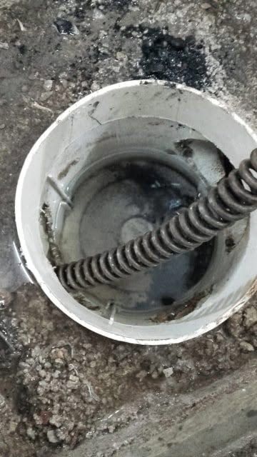 Abertura de una tubería de desagüe blanca en el hormigón, con un cable negro enrollado en el interior.