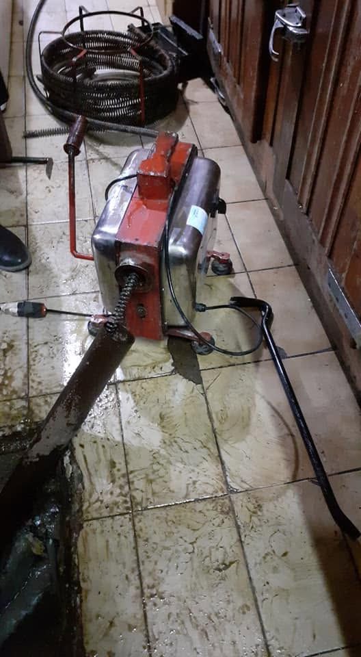 Máquina industrial roja sobre un suelo de baldosas, con mangueras y cables en un espacio de trabajo interior estrecho
