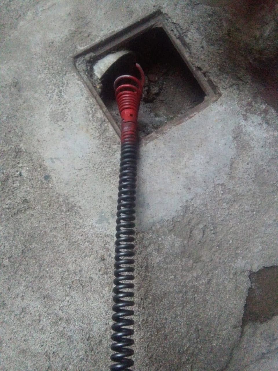 Manguera corrugada roja y negra que sale por una abertura cuadrada en un muro de hormigón