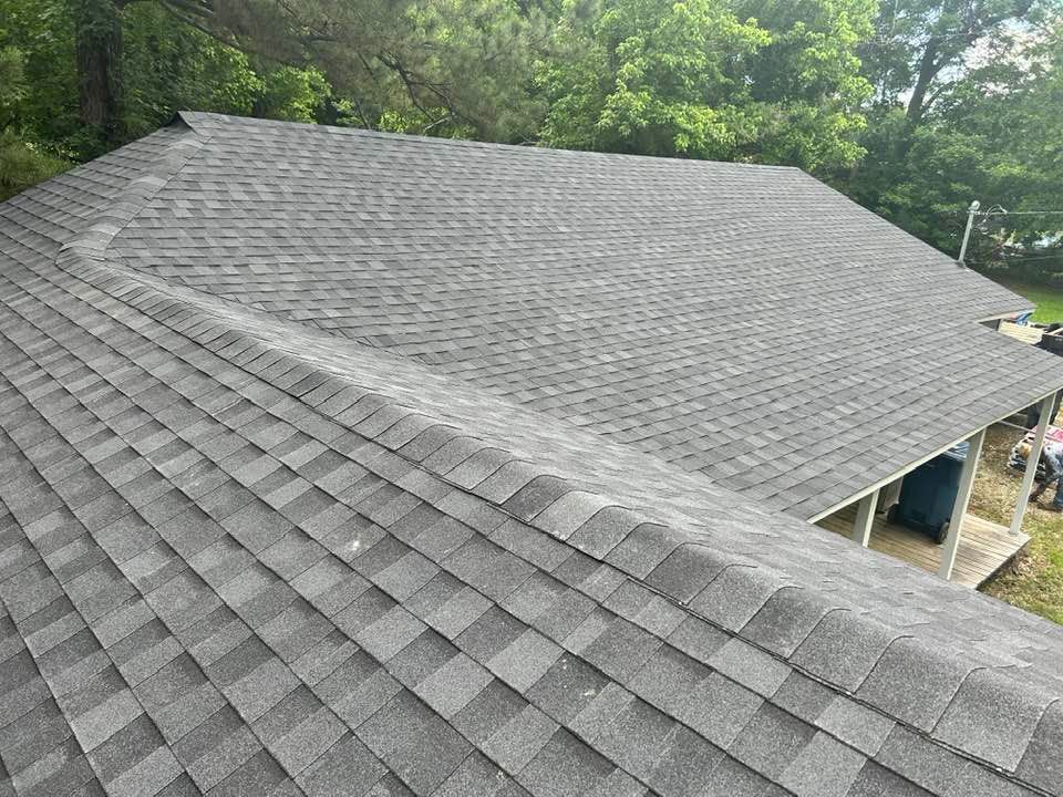 Gray asphalt shingle roof on a house, angled view, with trees in the background.