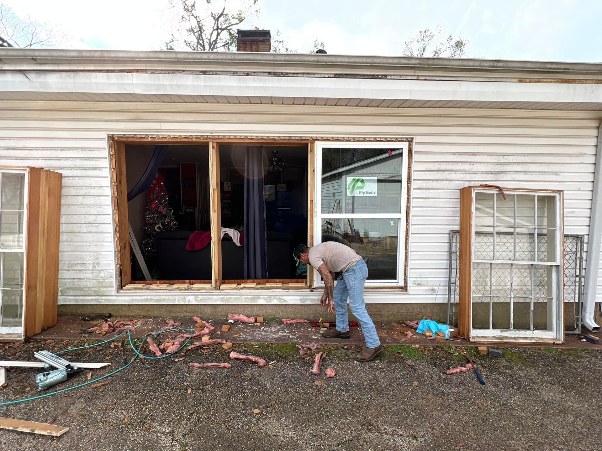 Person removing window from a white house. Debris and old windows on the ground.