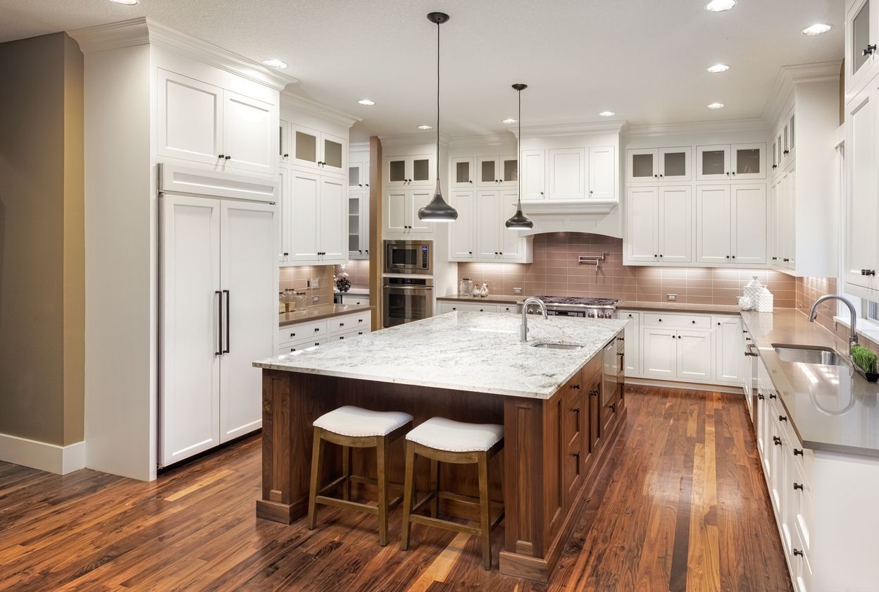 Spacious kitchen with white cabinets, a wooden island, and hardwood floors. Two stools sit at the island.