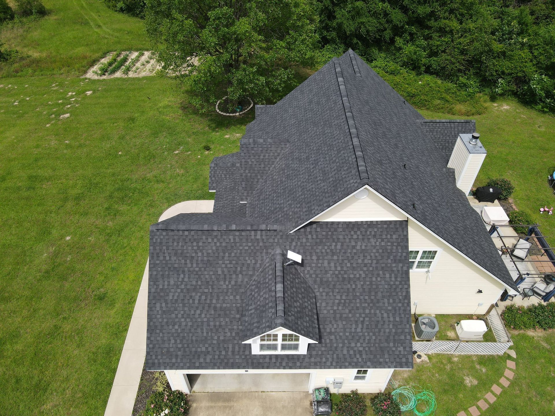 Aerial view of a house with a dark gray roof surrounded by green grass and trees.