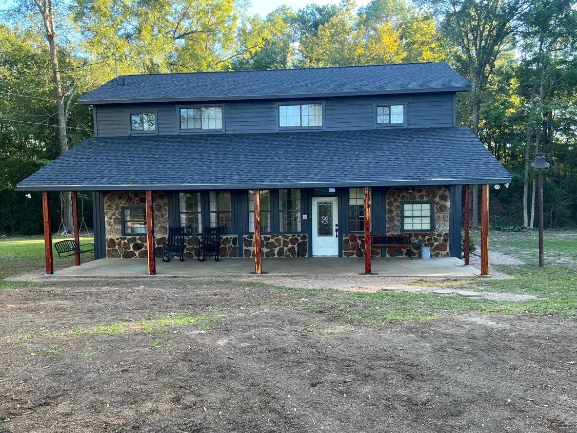 A large house with a porch in the middle of a field.