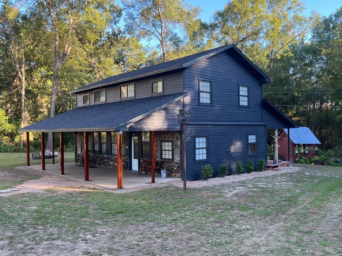 A large black house with a porch in the middle of a field.