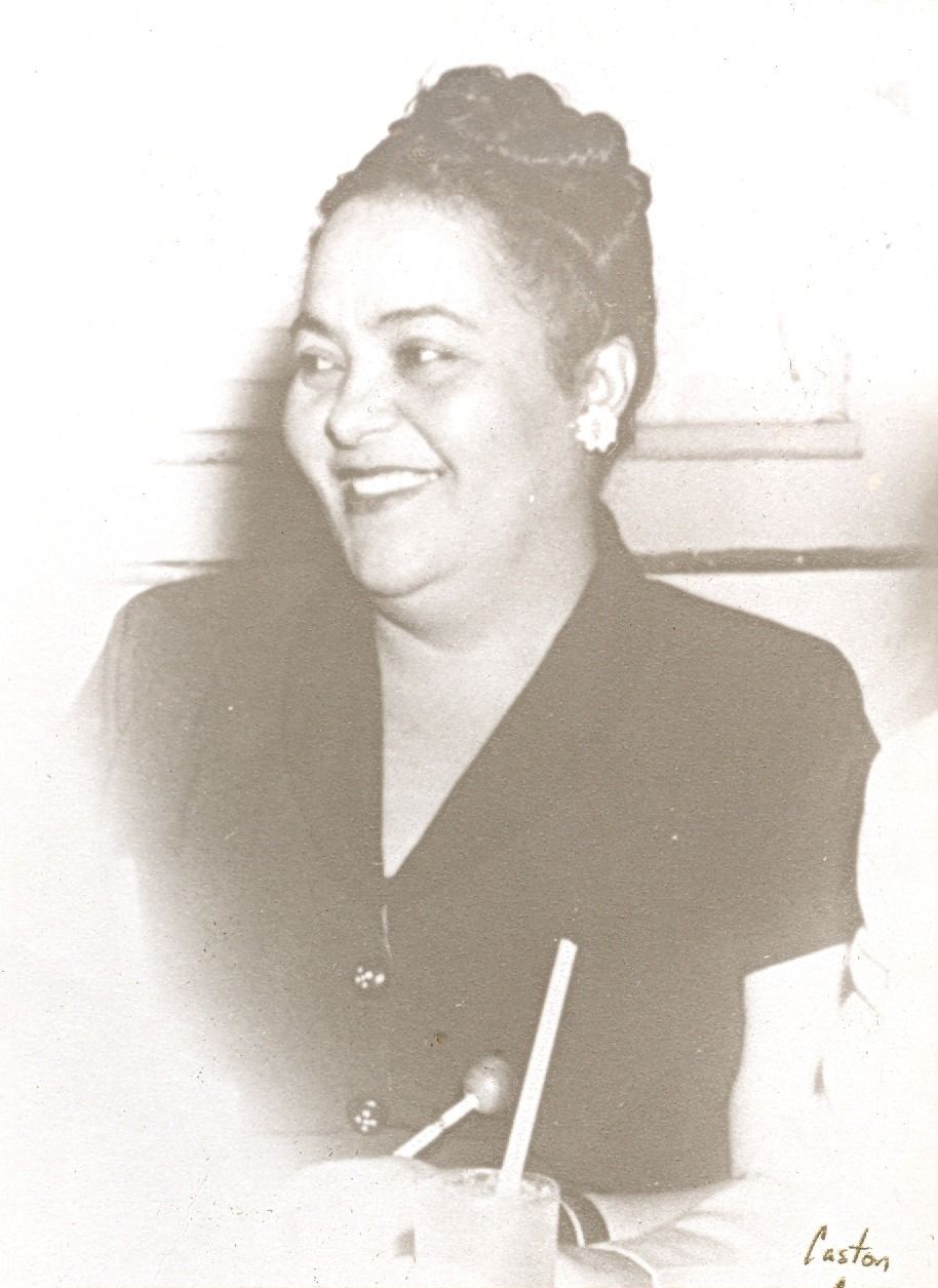 Smiling woman seated indoors, wearing a dark blouse, with a drink and straw in front of her.