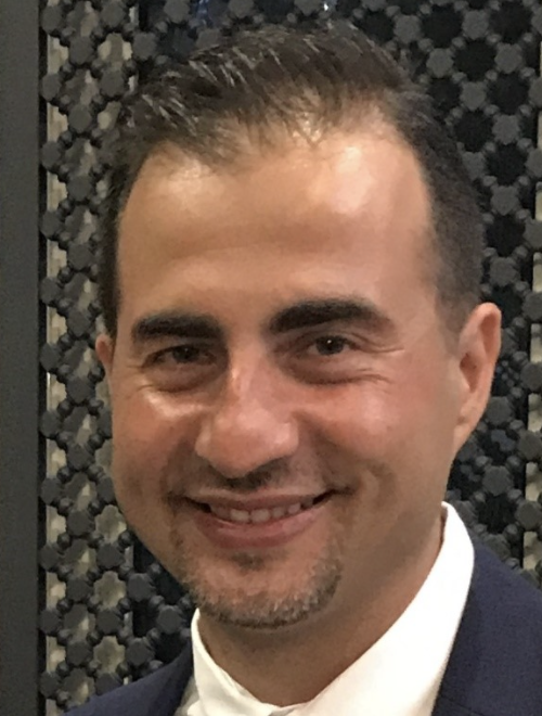 Portrait of a smiling man in a dark suit against a patterned background