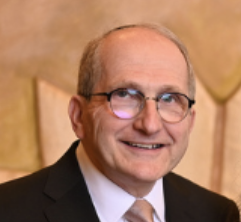 Portrait of a smiling man in glasses and a dark suit against a warm beige background