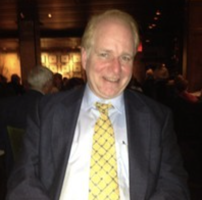 Smiling man in a dark suit and yellow tie at a dimly lit indoor event