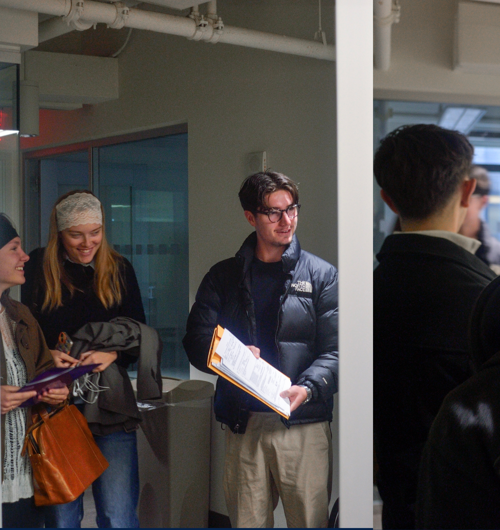 People standing in a hallway, smiling and holding papers and folders.