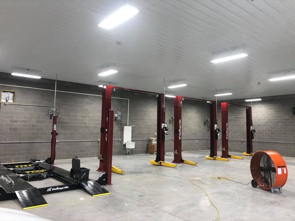 An empty auto repair shop with red lifts, concrete floor, and a large fan.