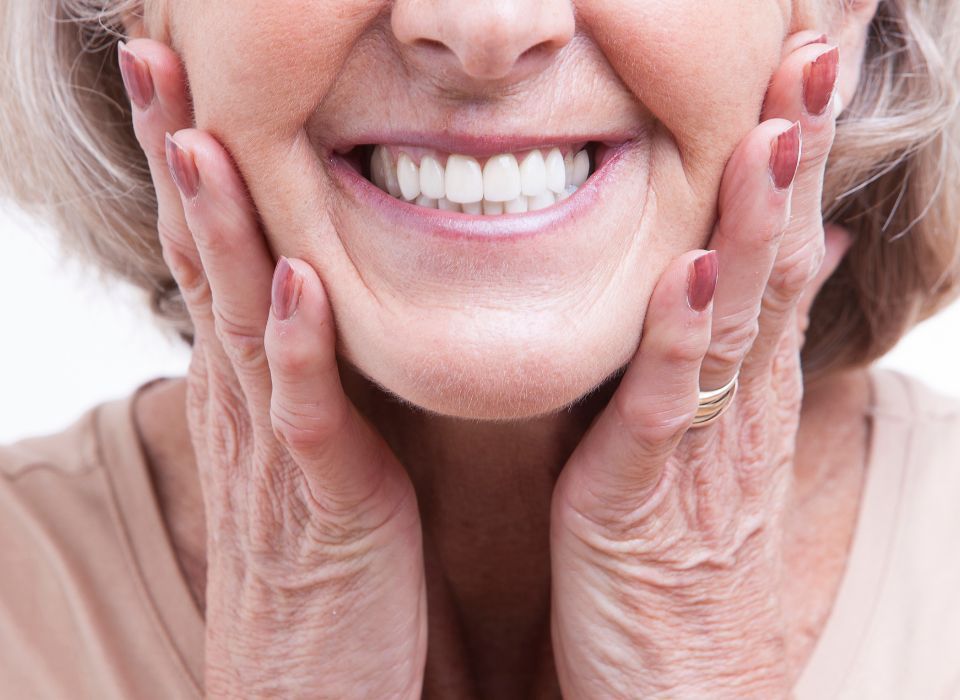 Smiling person, hands on cheeks, showing teeth.