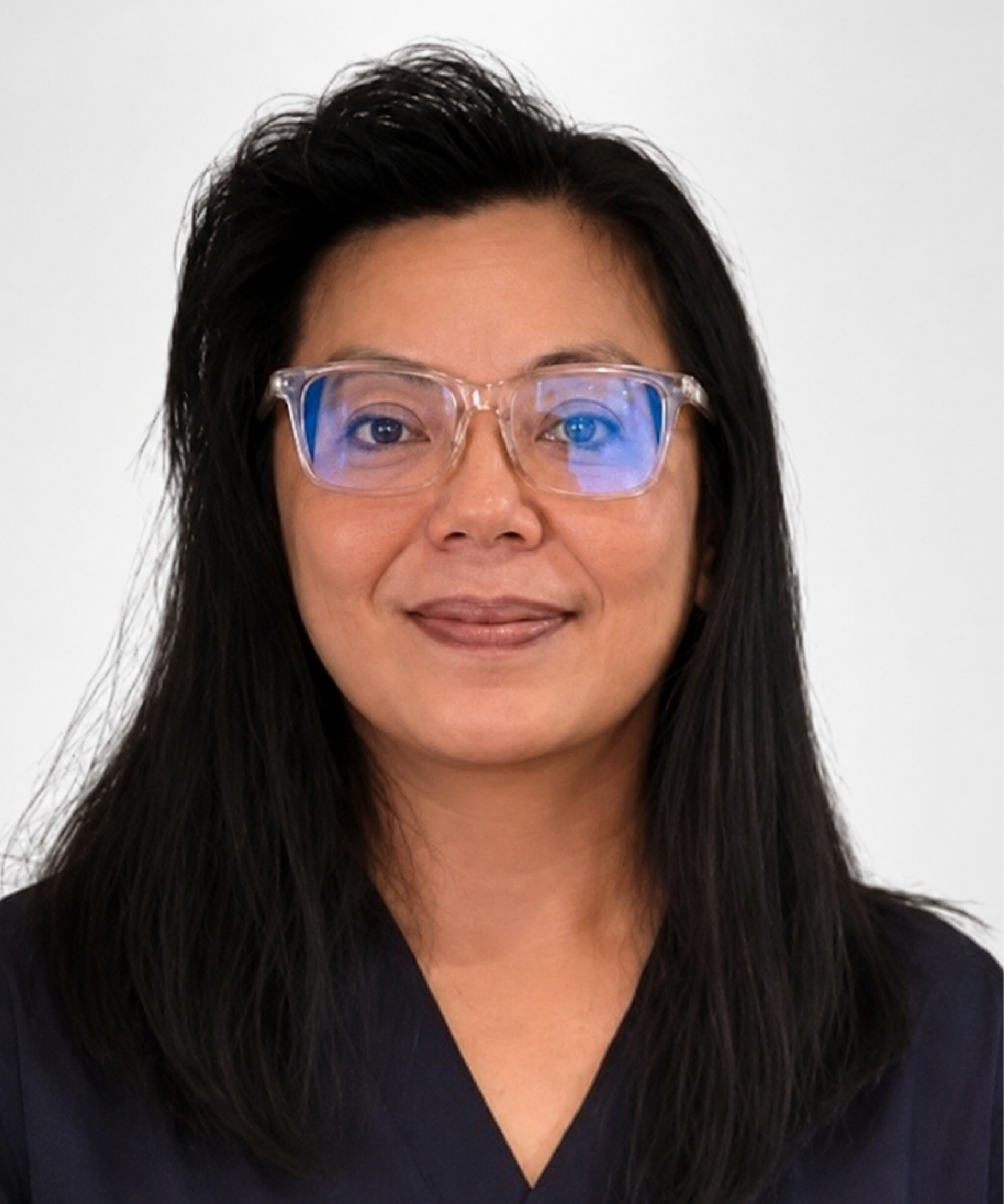 A woman wearing glasses and a scrub top is standing in front of a wall.