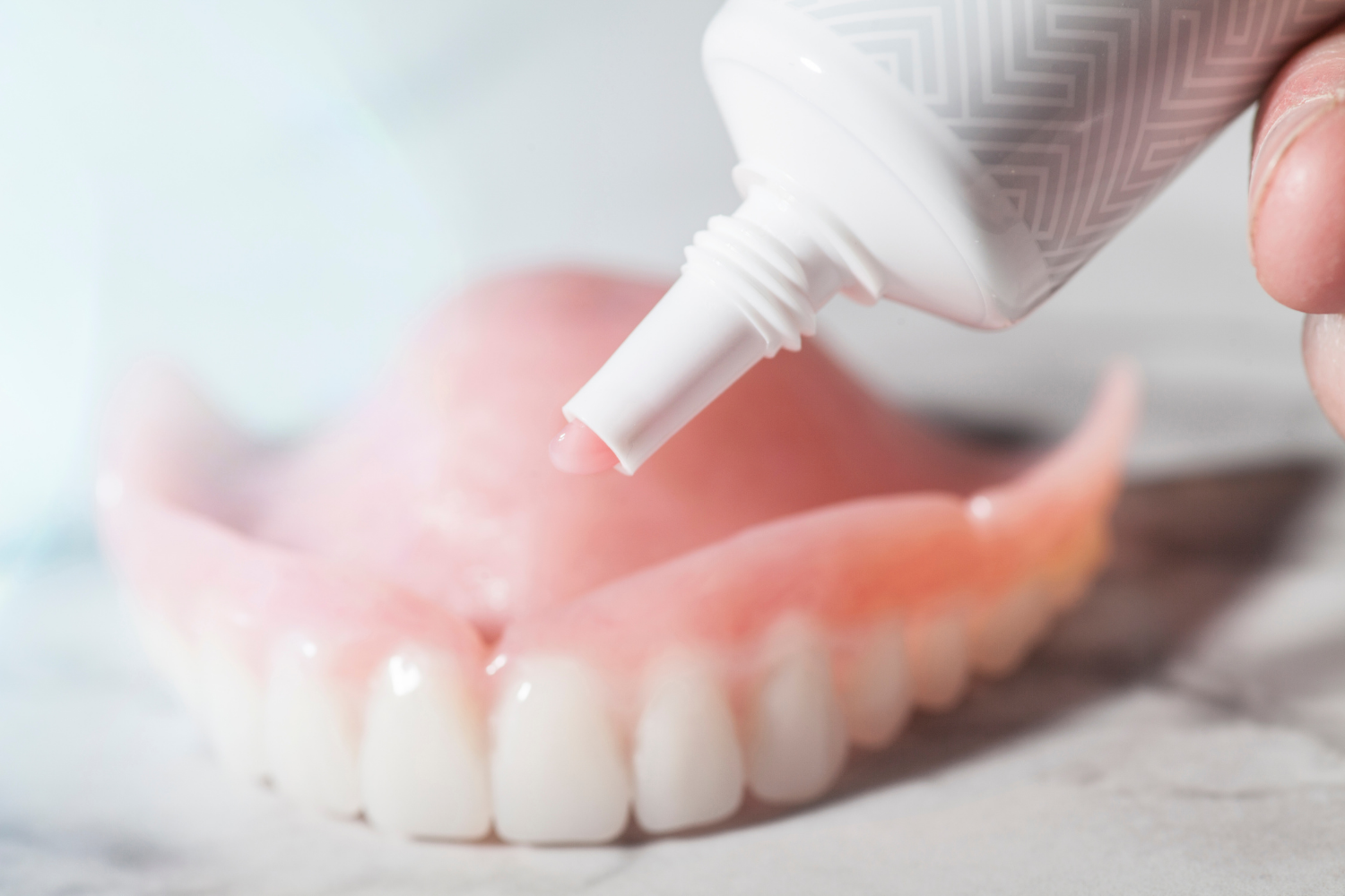 A person applying denture adhesive from a tube onto a set of dentures.