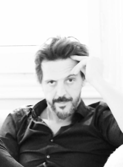 A man with a beard is sitting on a couch with his hand on his head.