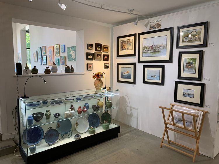 A room with a glass display case and paintings on the wall.