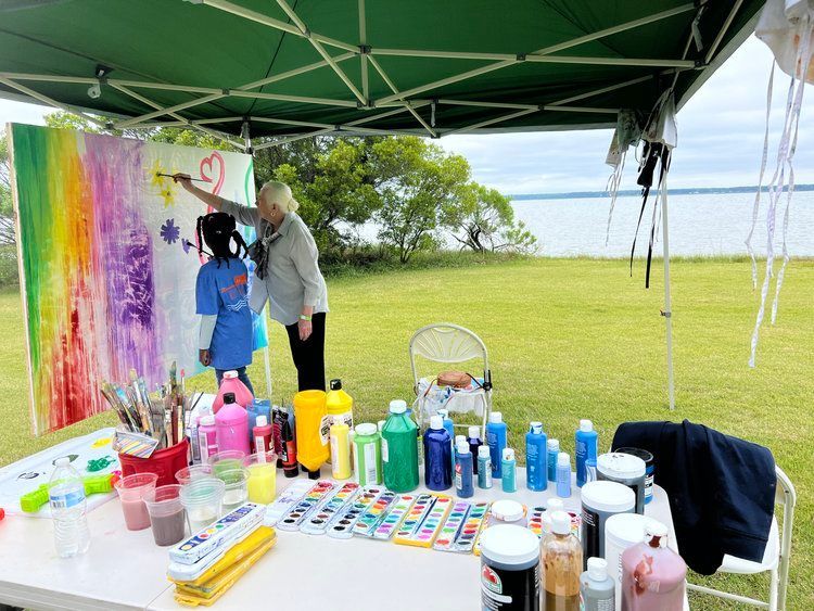 A woman is painting a picture with a child under a tent.