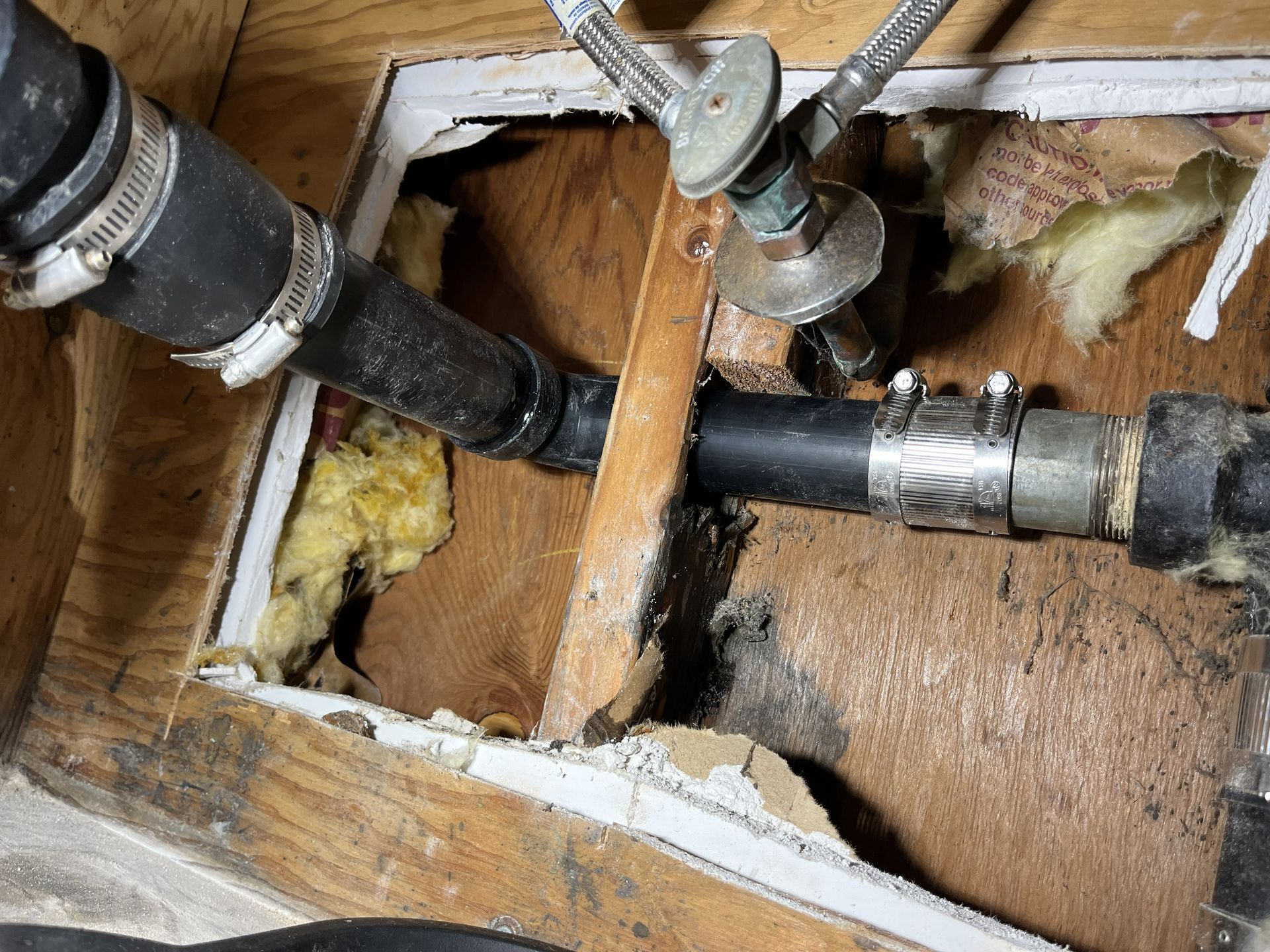 Exposed plumbing pipes and fittings inside a damaged wall with yellow insulation visible.