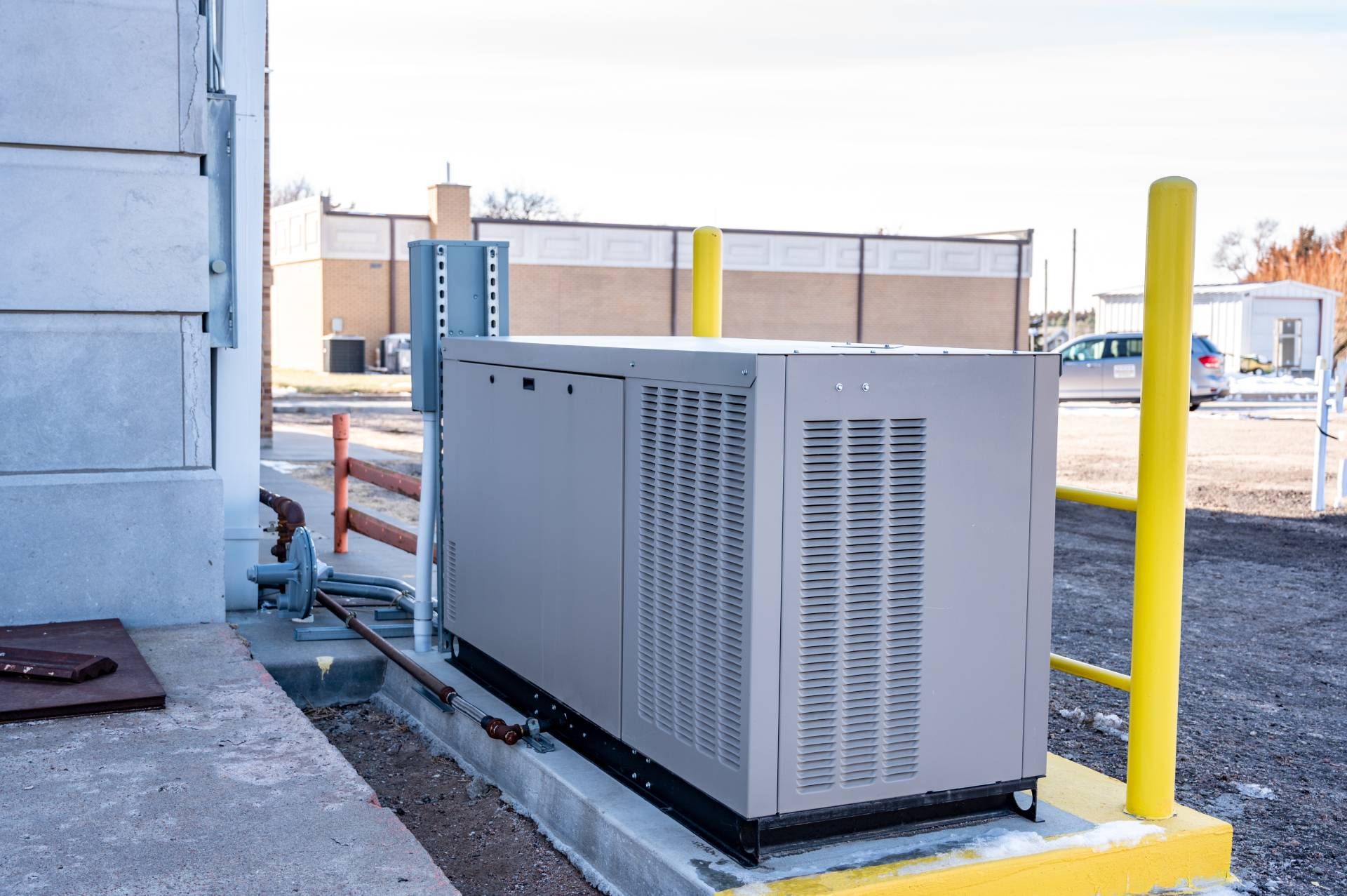 A commercial standby generator outside of a local business near a pair of yellow poles