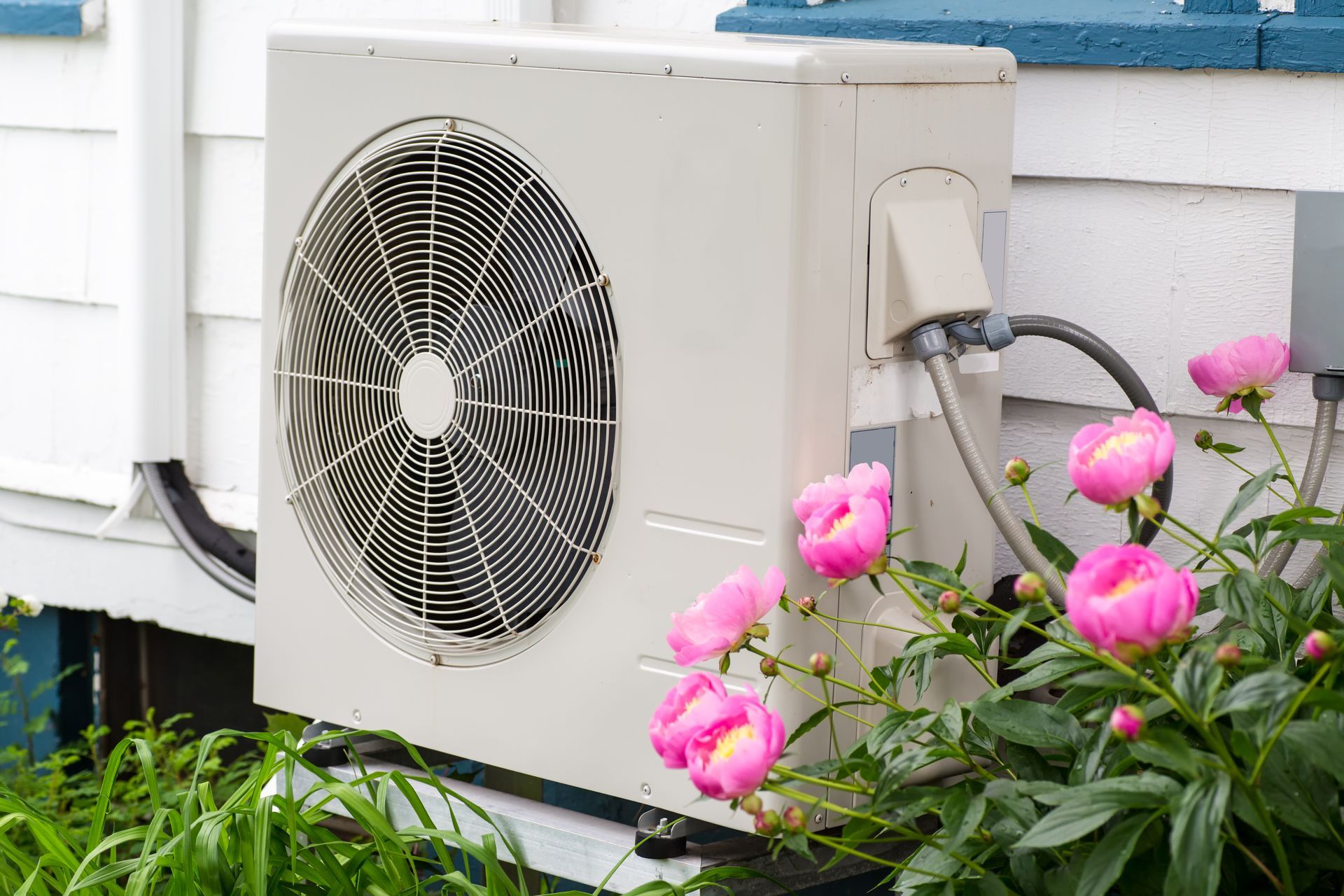 A heat pump near Somerset, KY, outside a residential home with pink flowers nearby