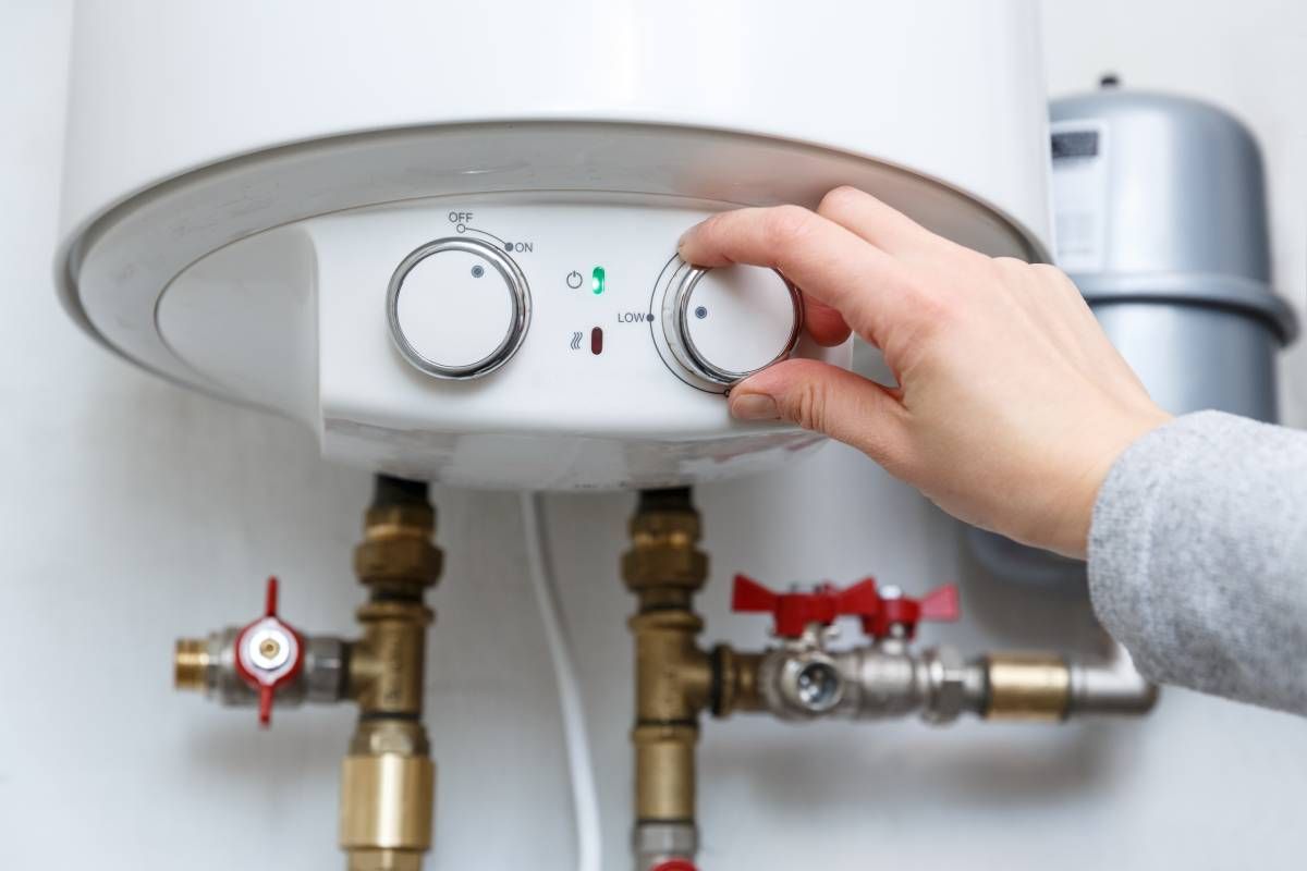 A homeowner's hand turning down the temperature on their water heater using a dial
