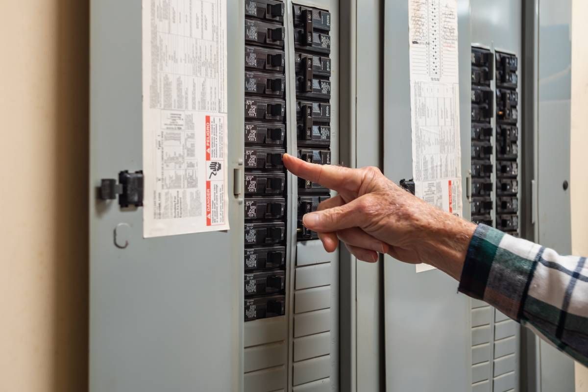 A homeowner's hand turning off power for an electrical outlet with their home's circuit breaker panel
