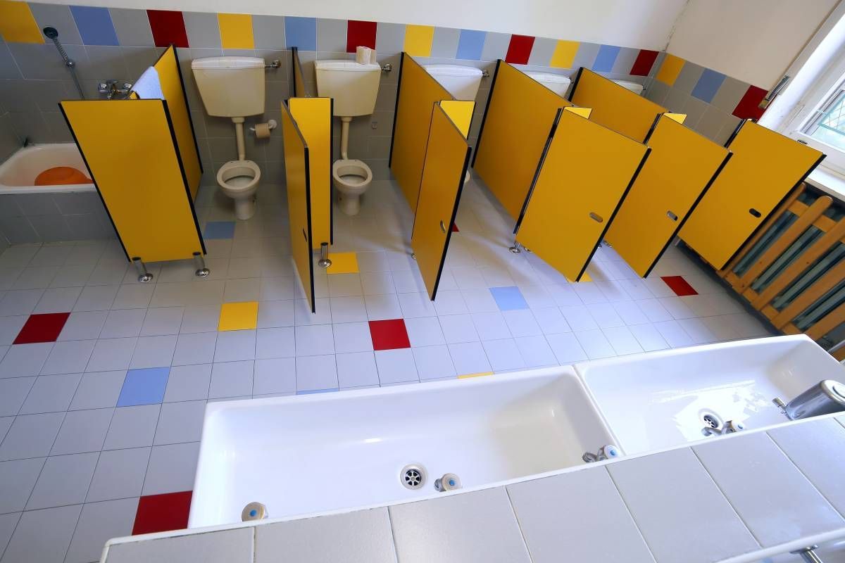 An elementary school bathroom with bright yellow stall doors and red, blue, yellow, and gray tiles near Somerset, KY