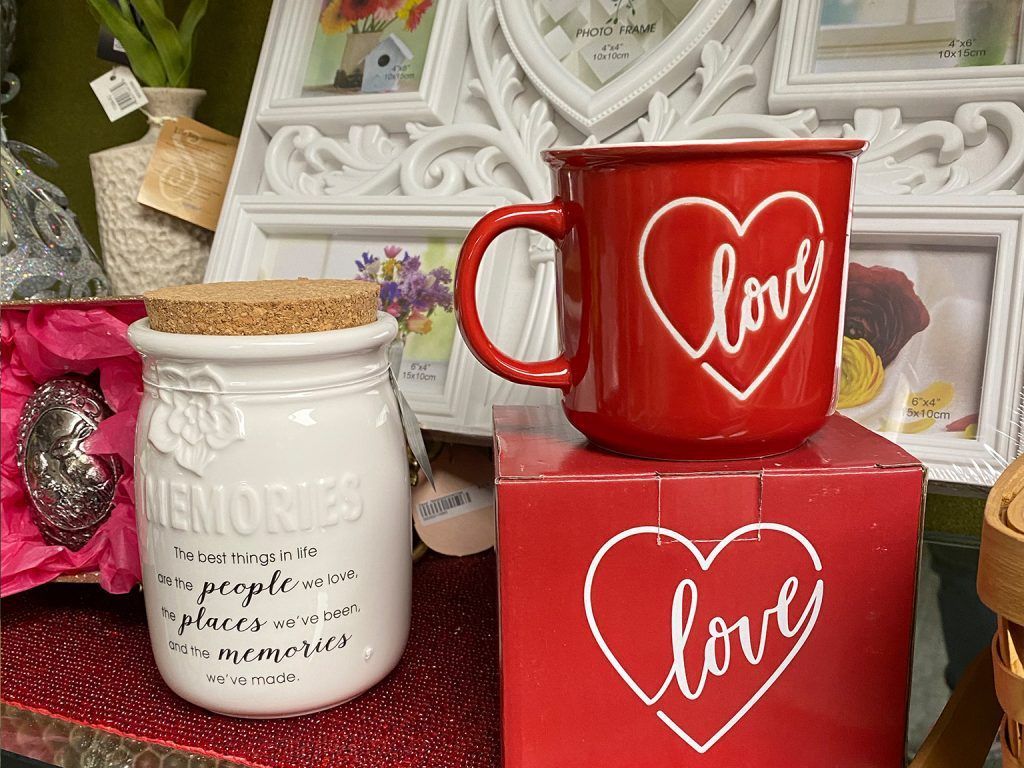 Red and white “love” mugs and a cream jar on decorative boxes with flowers in the background