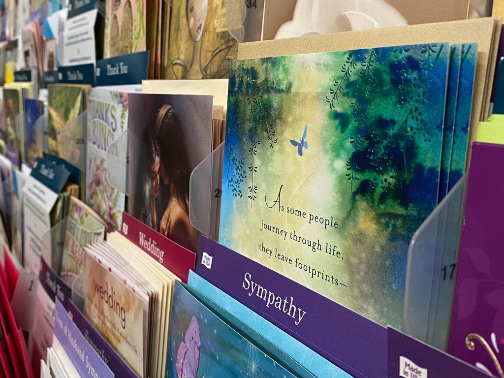 Greeting cards displayed on a store rack, featuring colorful scenic and abstract designs