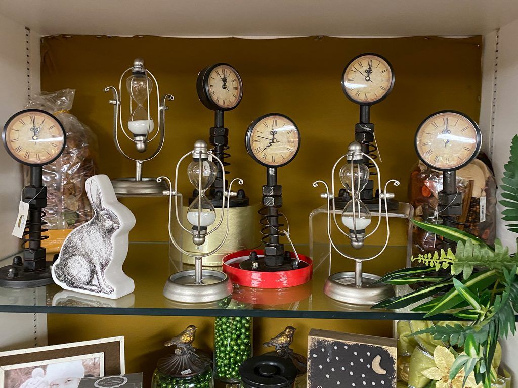 Shelf of vintage analog thermometers, gauges, and lamps with a rabbit figurine and plants arranged indoors