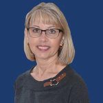 Portrait of a smiling woman with blonde hair and glasses against a blue background