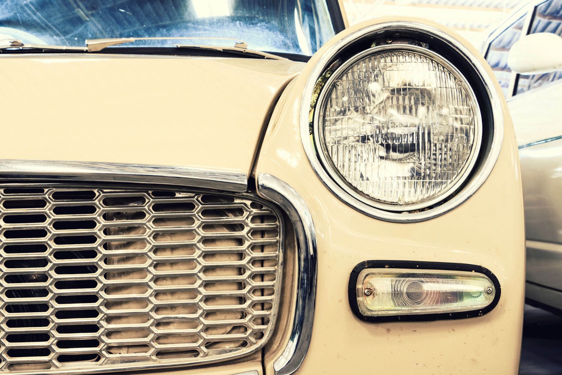 Vista frontale di un'auto d'epoca color crema con griglia cromata e faro rotondo.