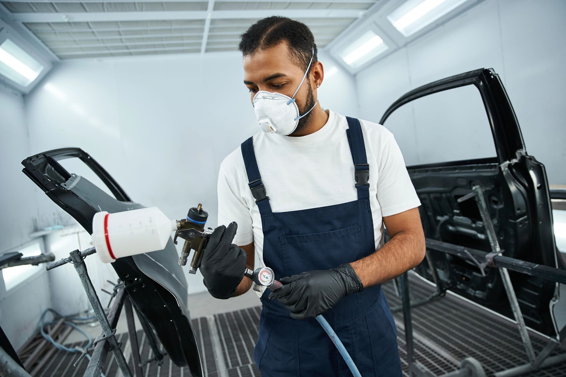 Un uomo in un garage ispeziona la presa di ricarica di un'auto indossando guanti e mascherina.
