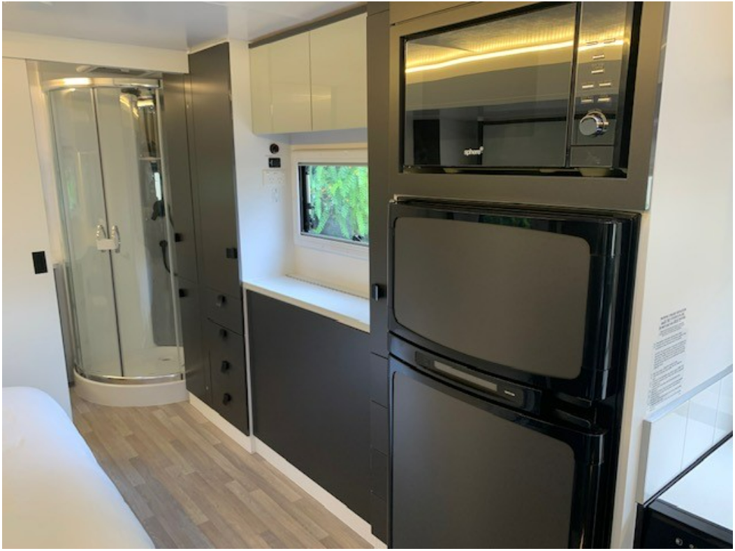A kitchen in a camper with a refrigerator , microwave , and shower.