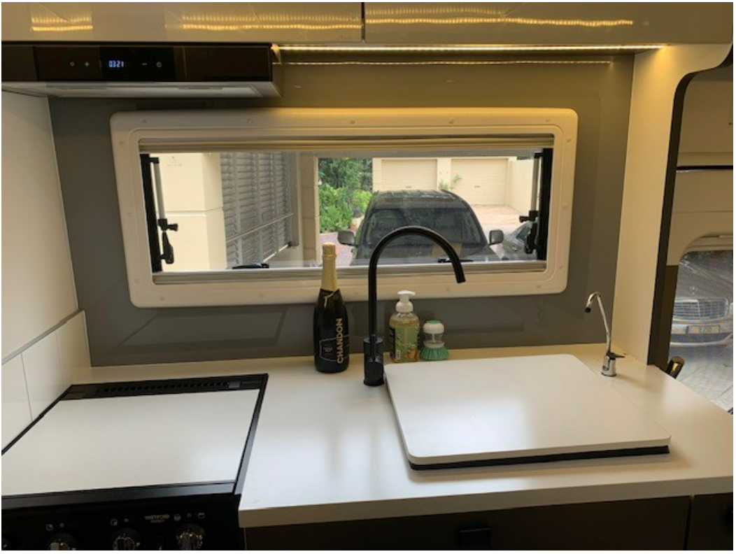 A kitchen in a camper with a sink , stove and window.