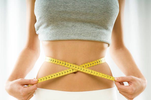 A woman is measuring her waist with a tape measure.