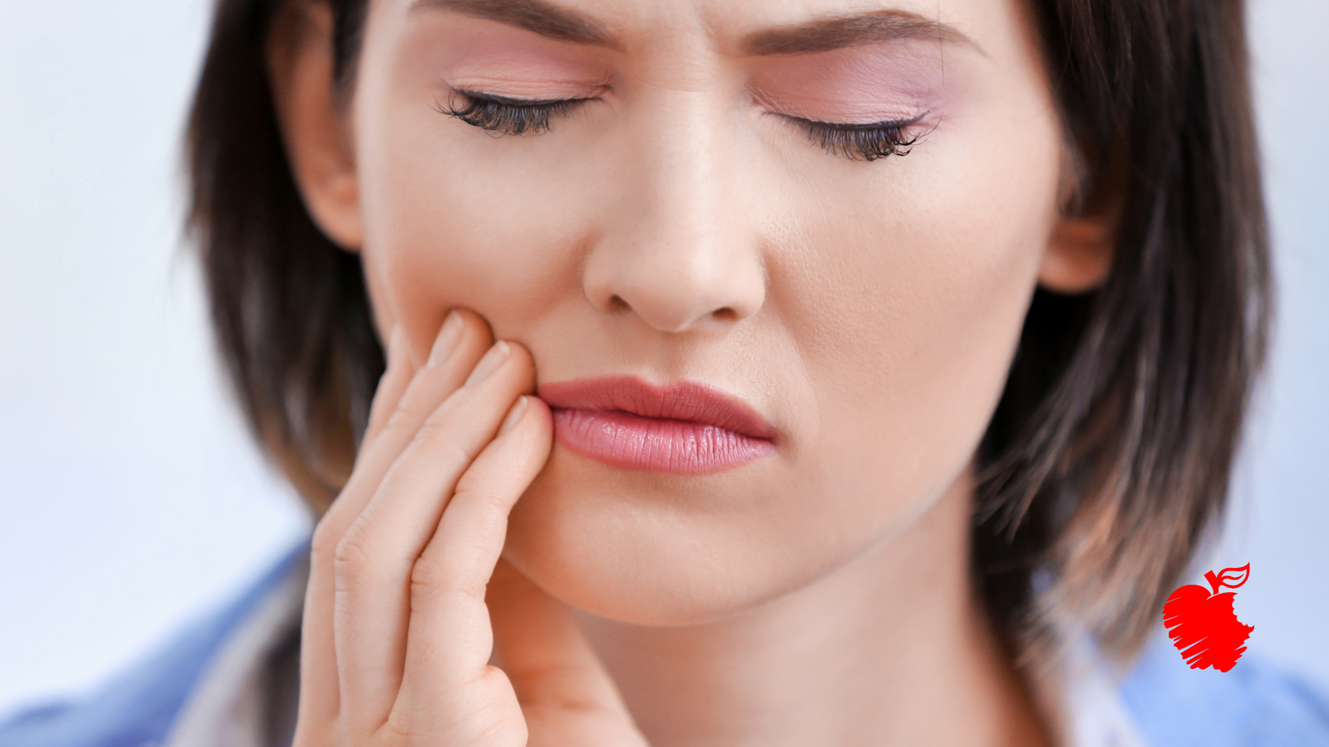 Woman with eyes closed, hand on jaw, showing a pained expression.