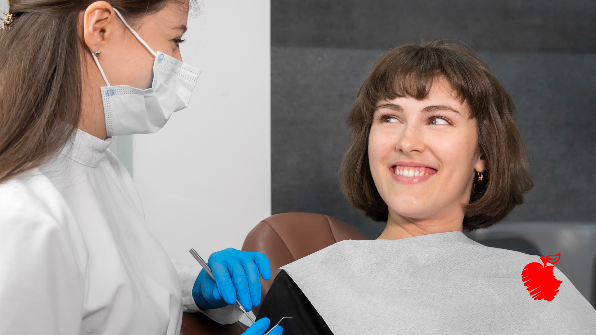 A woman is sitting in a dental chair while a dentist examines her teeth.