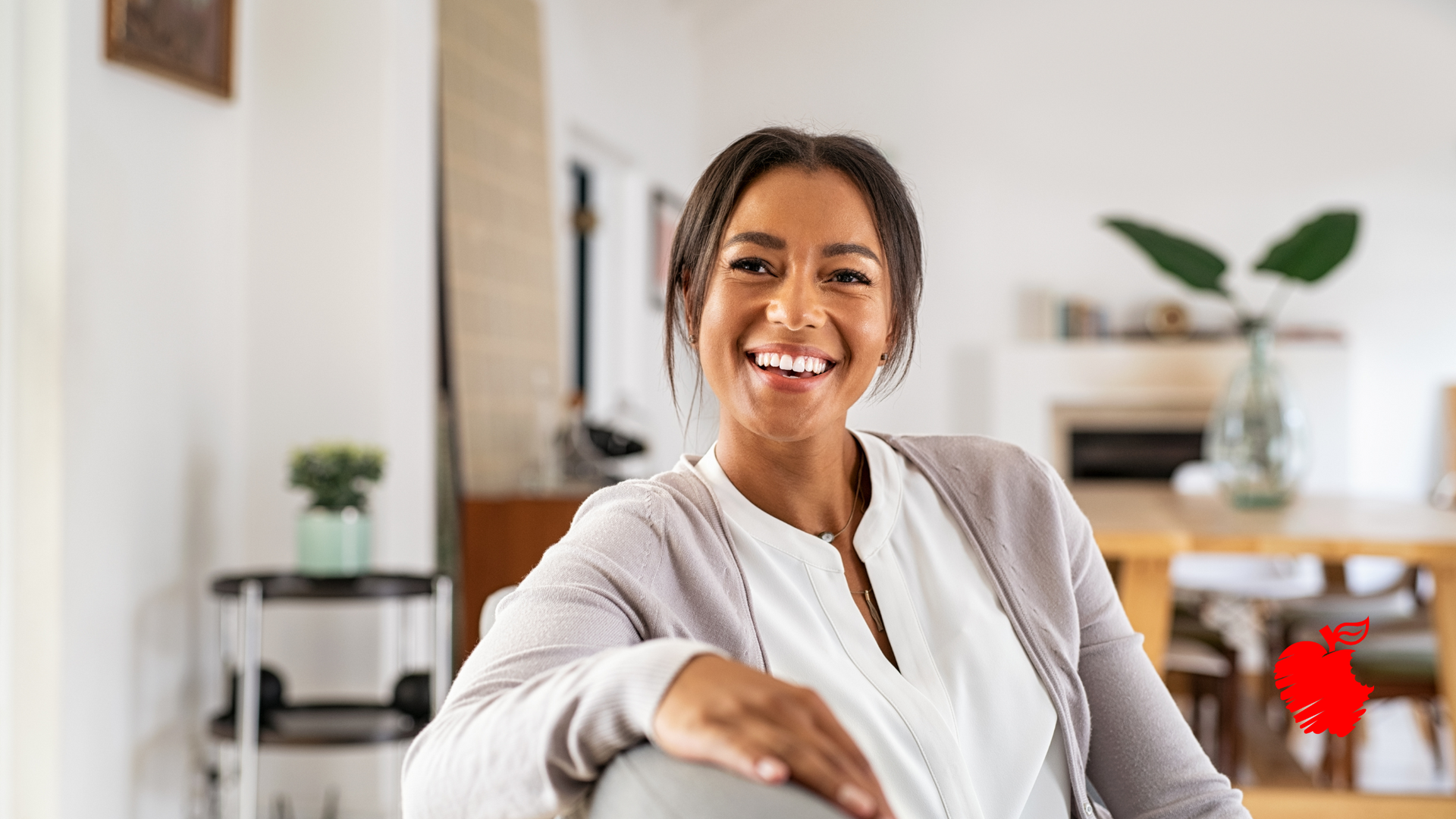 A woman is smiling while sitting on a couch in a living room.