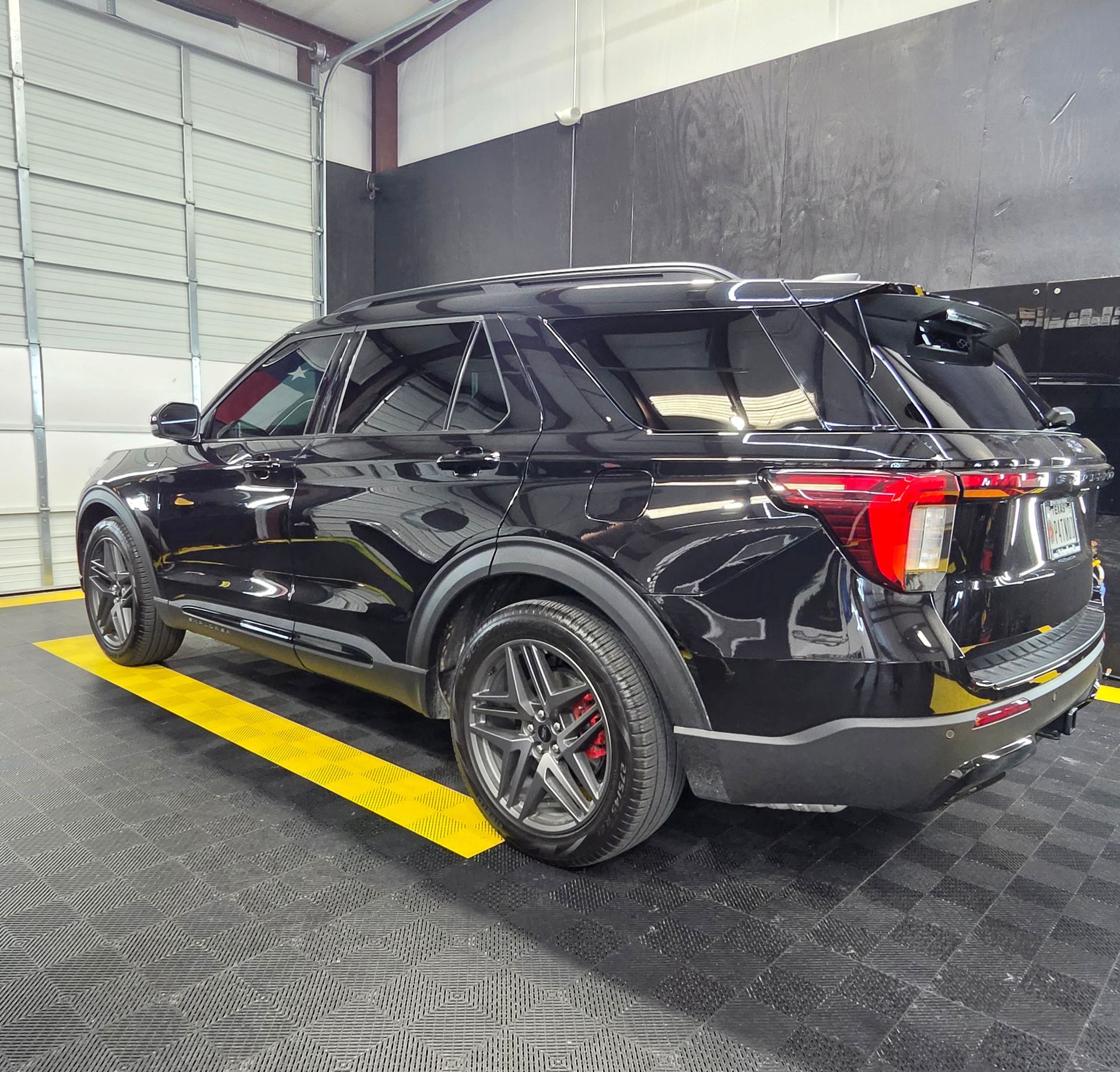 Black SUV parked in a garage, viewed from the rear side on a yellow marked bay.