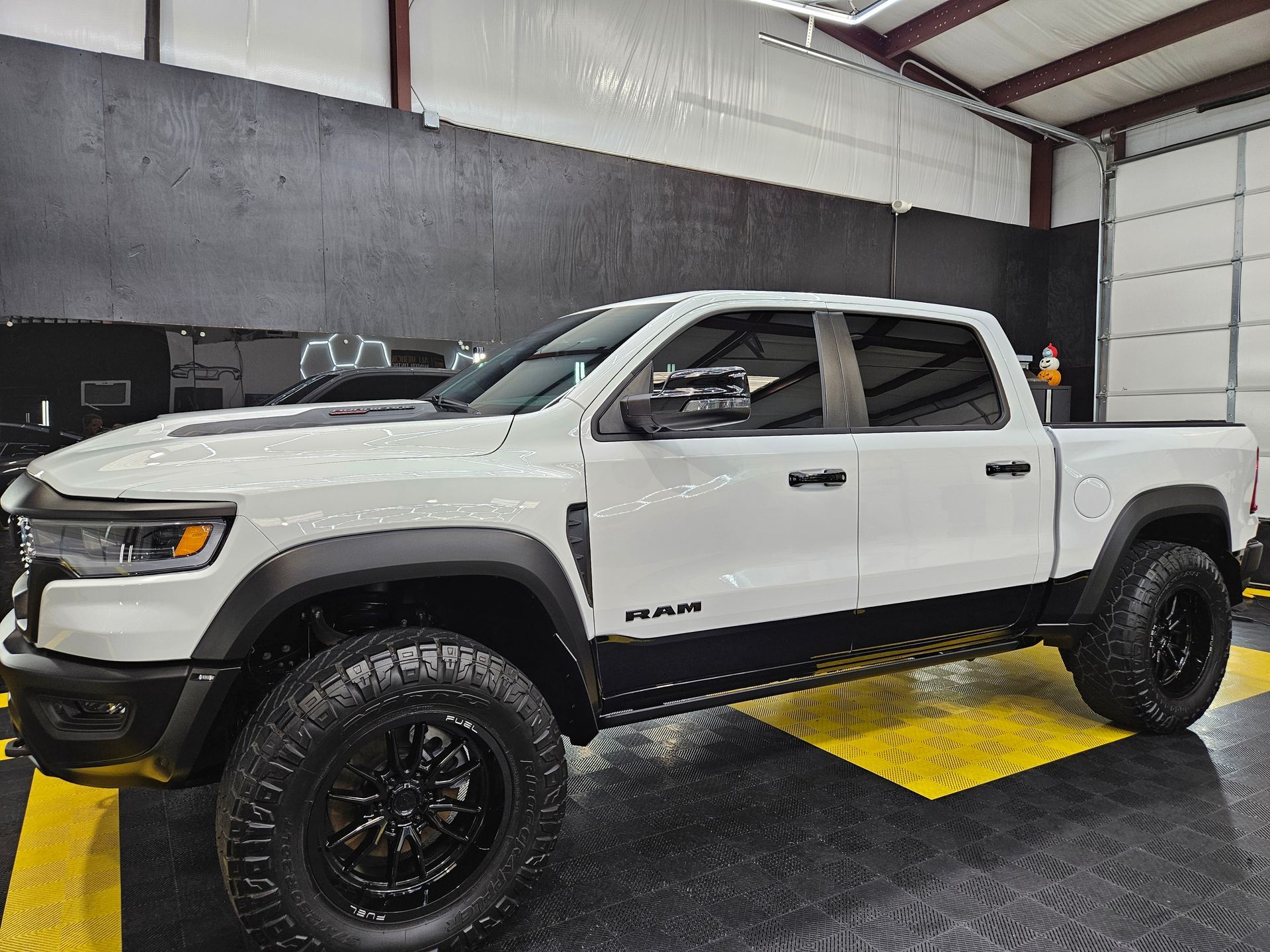 White lifted pickup truck with black wheels parked indoors on a yellow floor marking