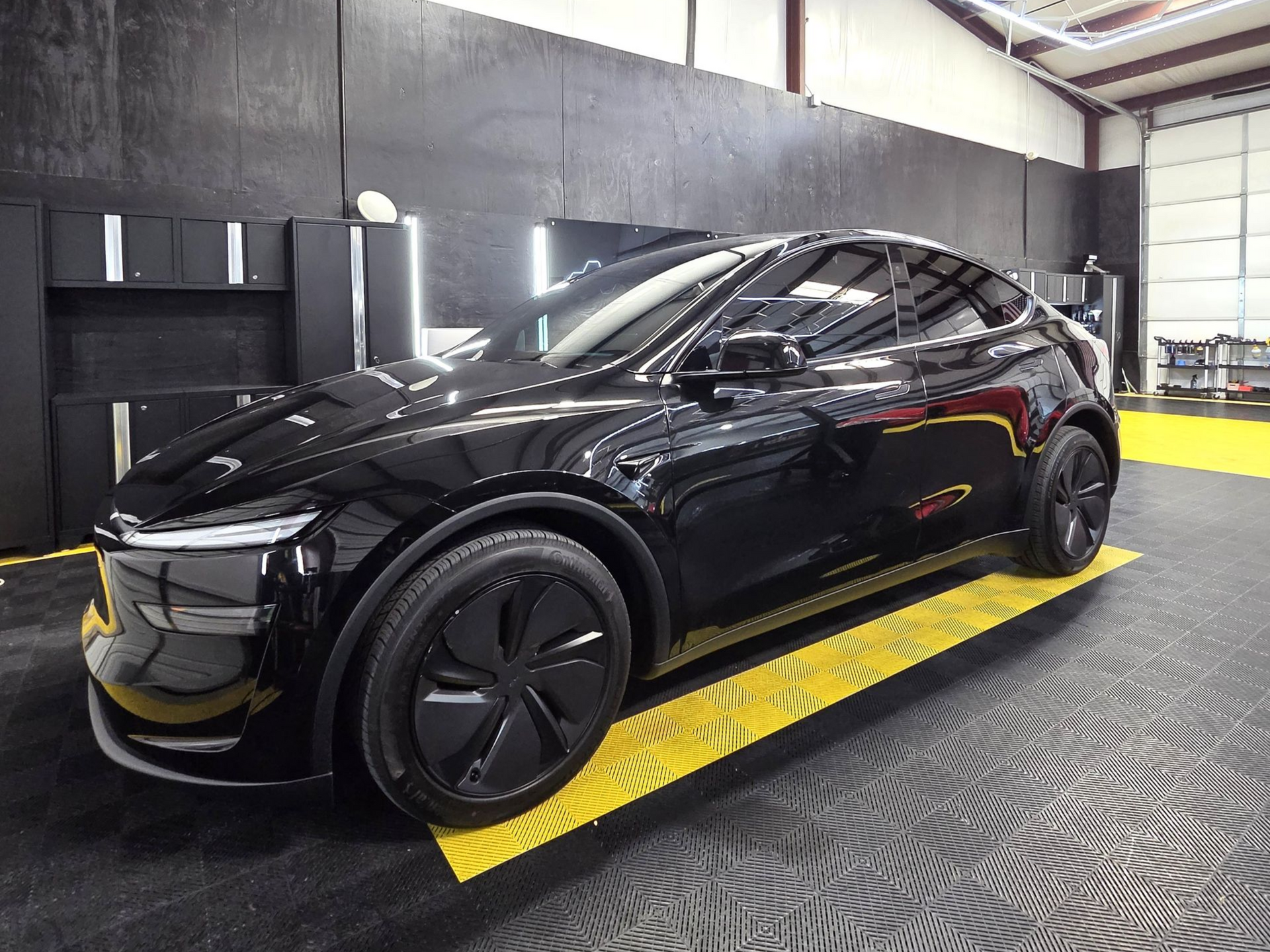Black sports car on a yellow platform in a garage or detailing bay
