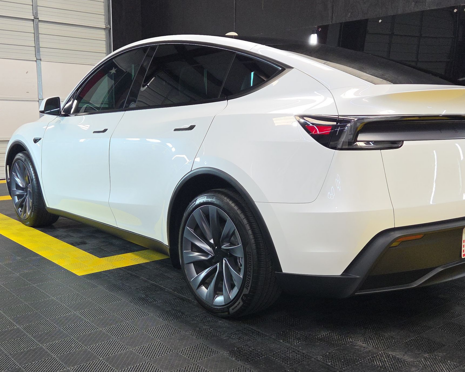 White Tesla SUV parked in a garage, viewed from the rear side